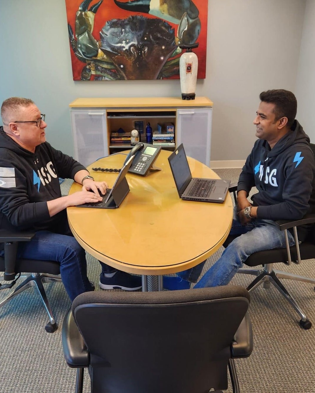 Two ISG teammates in branded hoodies working on laptops at a round office table